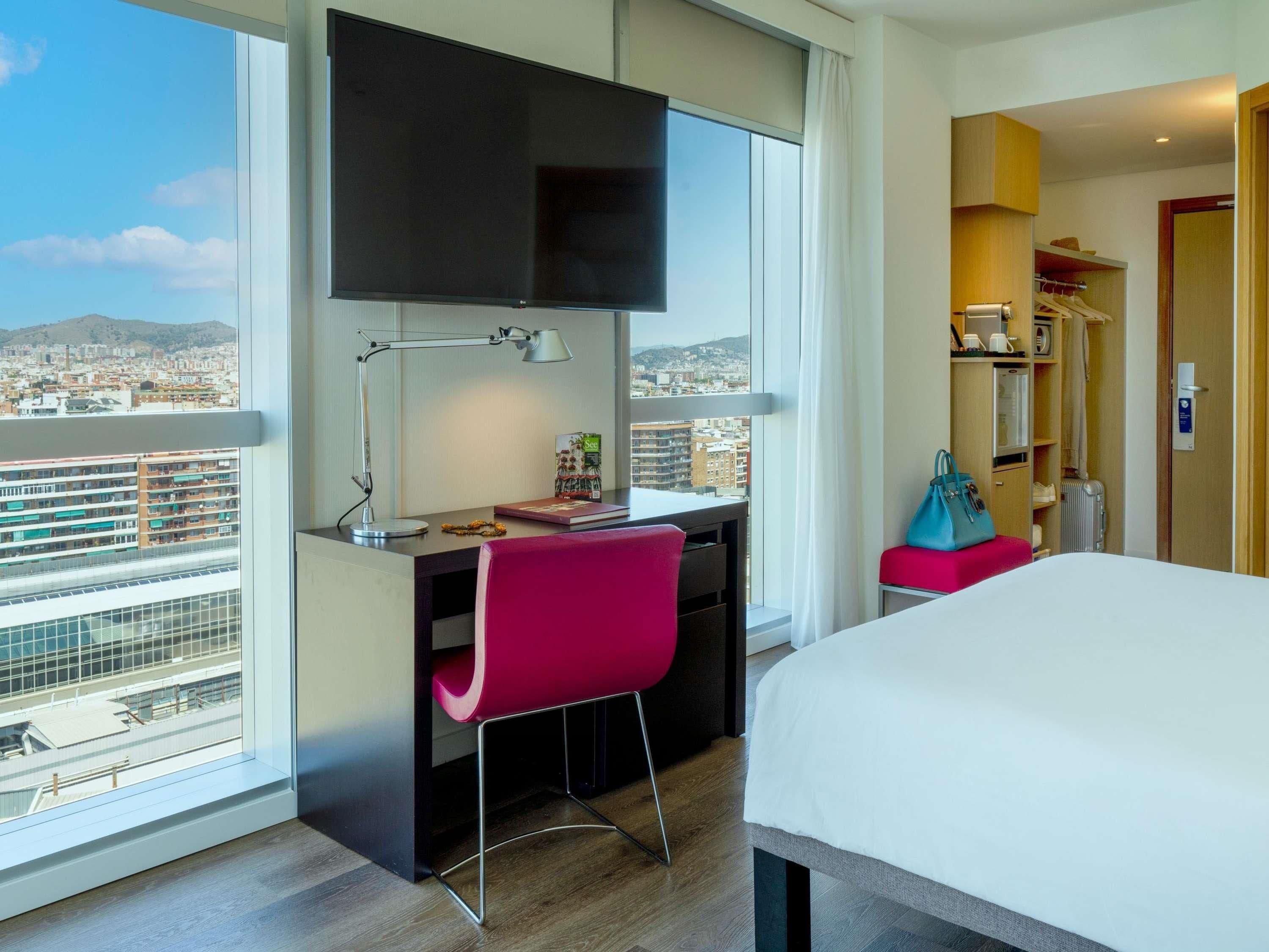 Une chambre d’hôtel équipée d’un bureau, d’une chaise, d’un lit et d’un téléviseur fixé au mur.