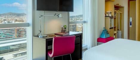 Una habitación de hotel con escritorio, silla, cama y televisor instalado en la pared.
