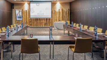 Un salón de conferencias con una larga mesa, sillas, una pantalla de proyector y una pared de bambú.
