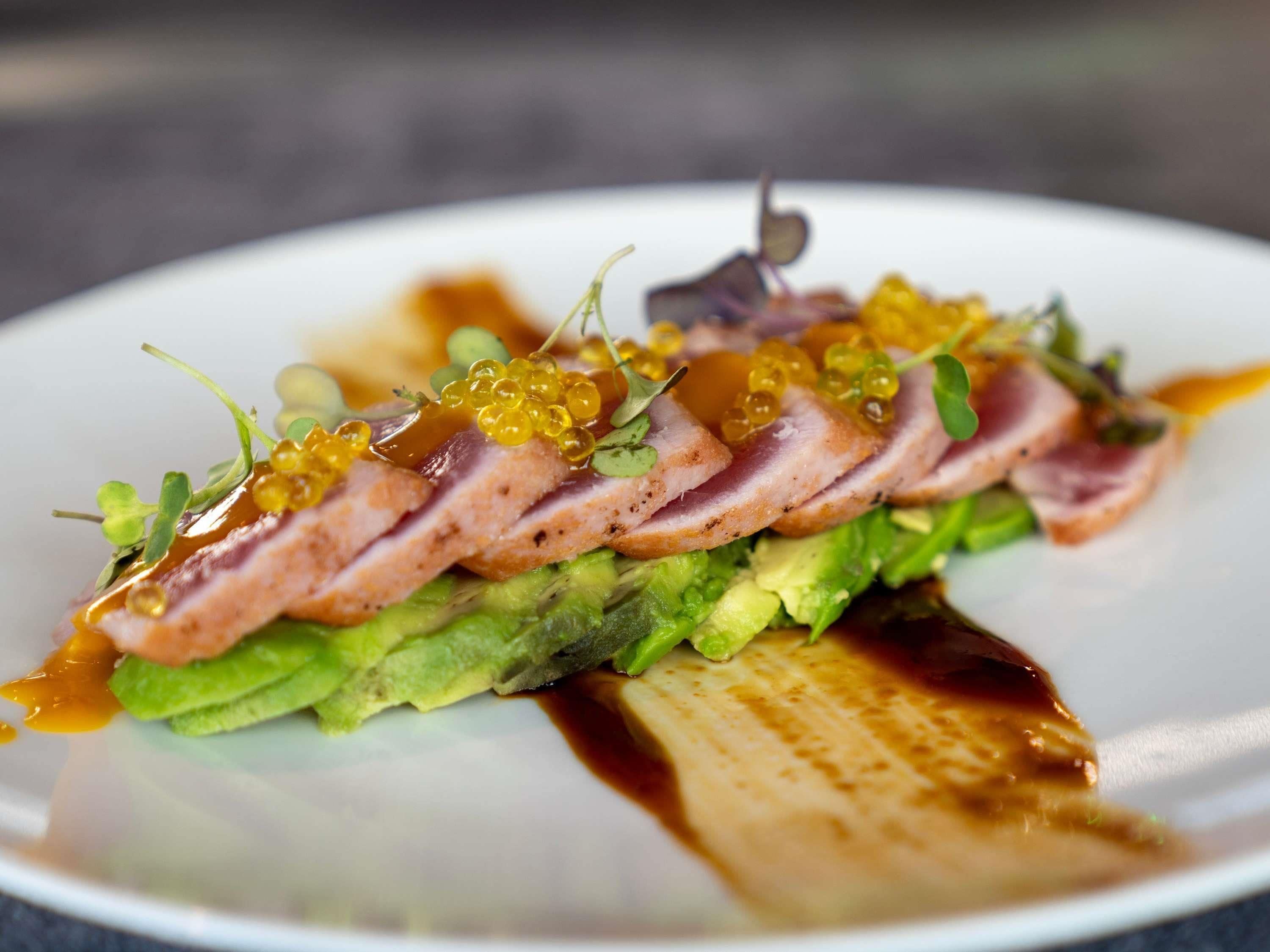 A plate of food with slices of meat, avocado, and caviar.