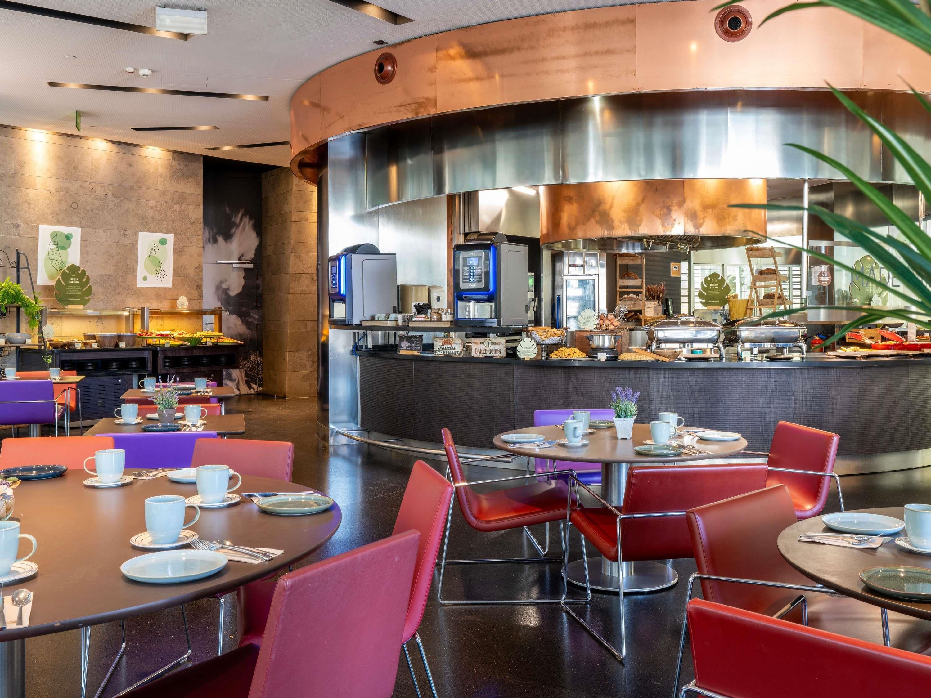 Een modern restaurant met ronde tafels, rode stoelen en een buffet met diverse gerechten.