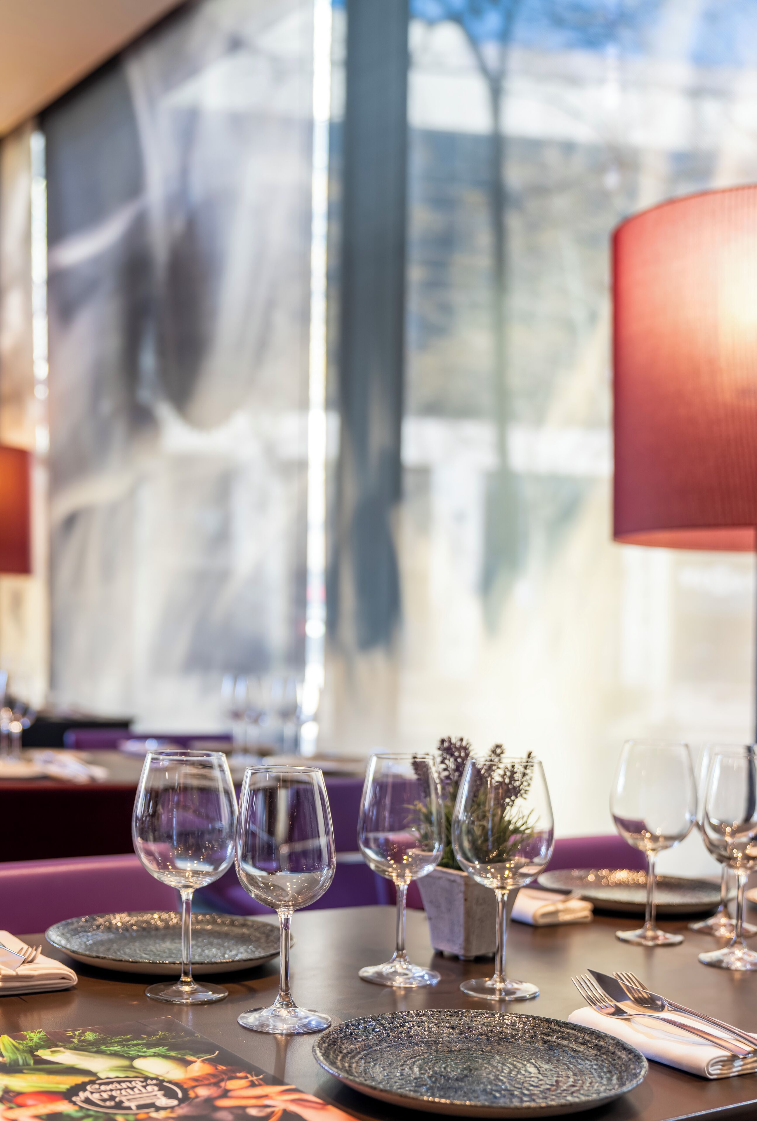 A dining table set with plates, glasses, and cutlery, with a window view in the background.