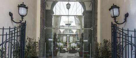 Un pasillo con suelo de piedra, techos abovedados y puertas de cristal que dan a una habitación amoblada.