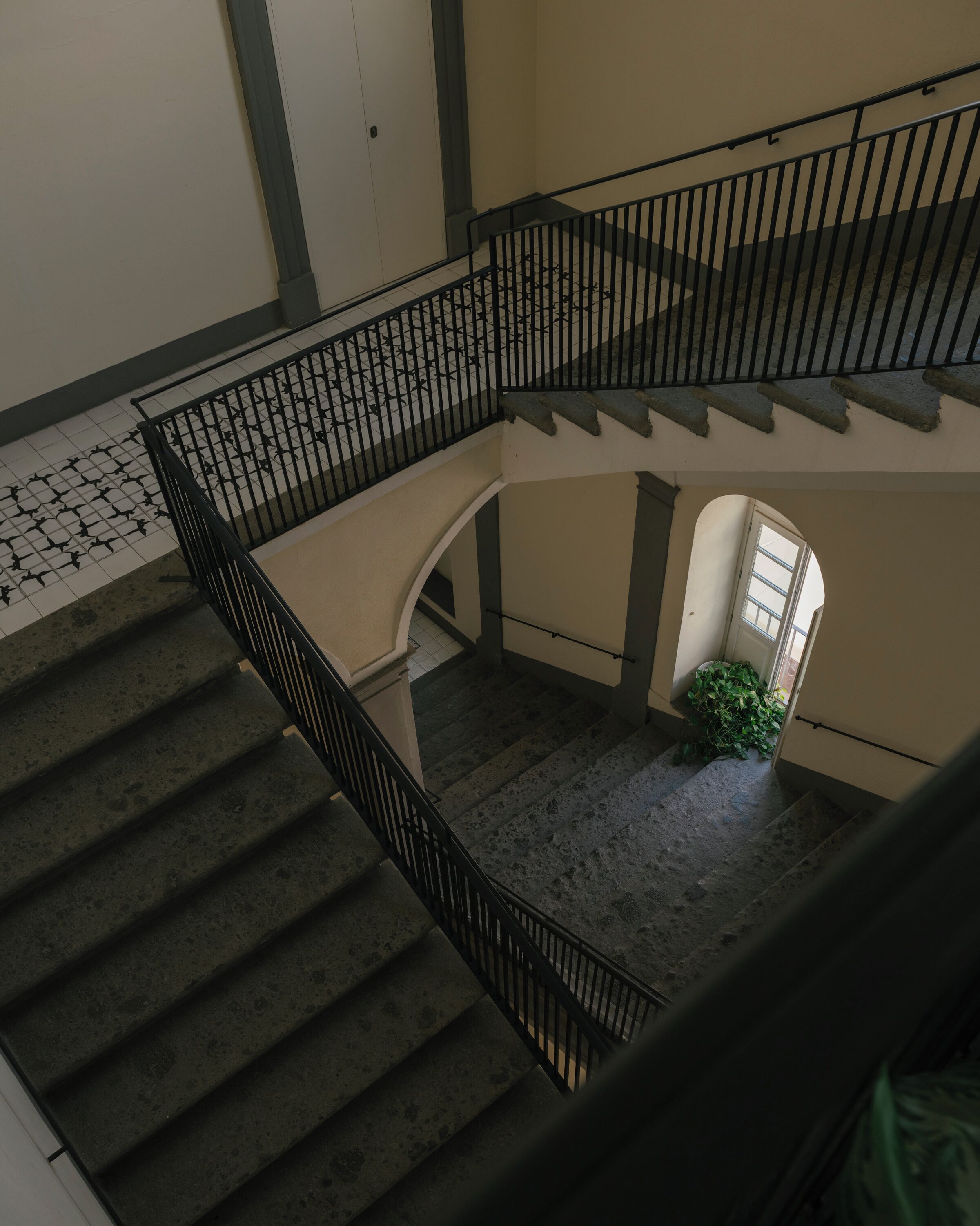 Un interior con varios niveles, una escalera, una planta pequeña y suelo de baldosas.