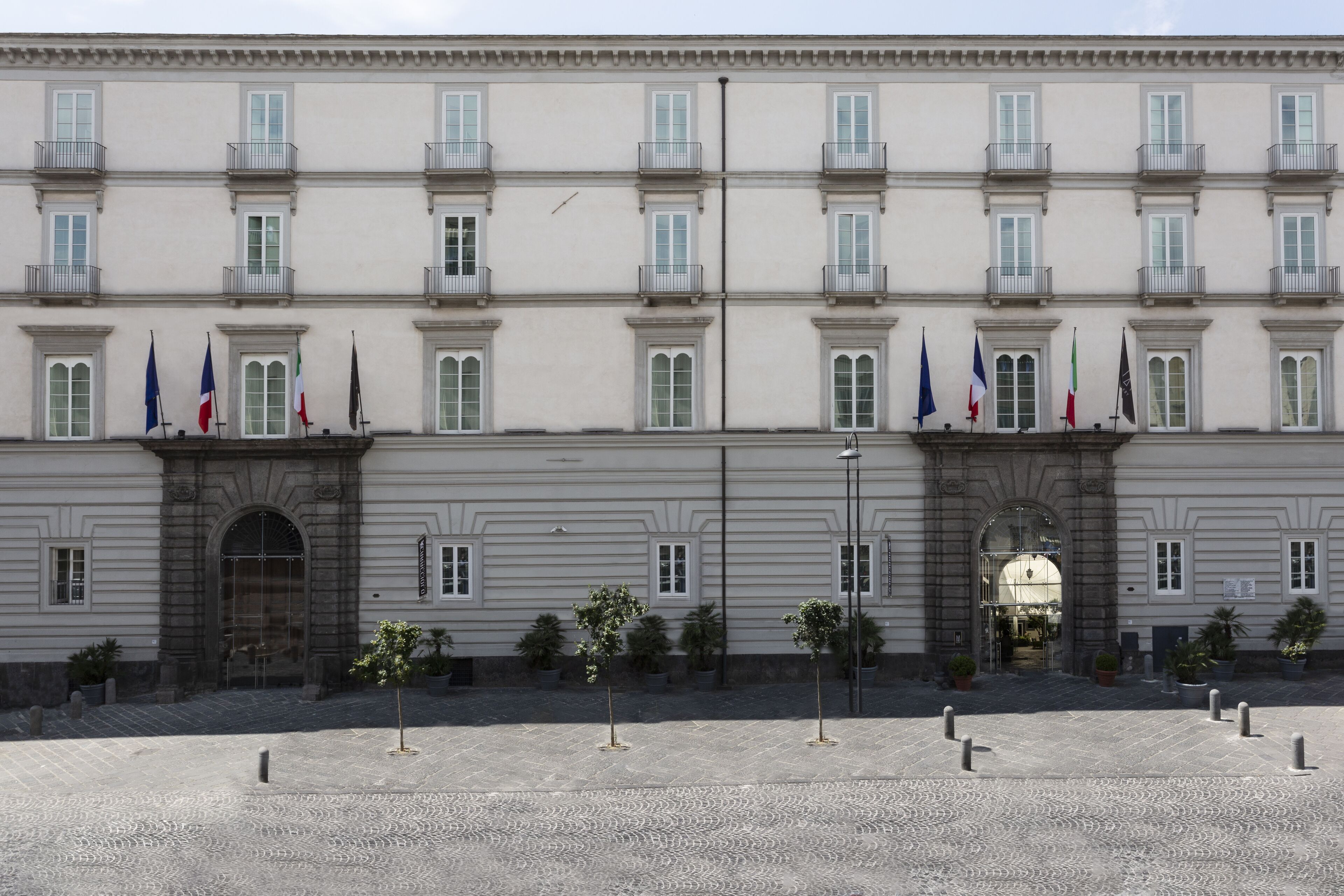 A large, historic building with multiple balconies and flags, featuring a symmetrical facade and a central entrance.