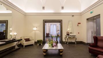 Una hall con una reception, un divano bianco, un divano rosso, un tavolino con vasi e uno specchio.