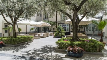 Zona salotto all'aperto con diversi tavoli e sedie, immersa nel verde e alberi.