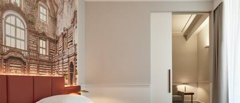 A hotel room with a large bed, a headboard with a mural, a nightstand, and a door leading to a bathroom.