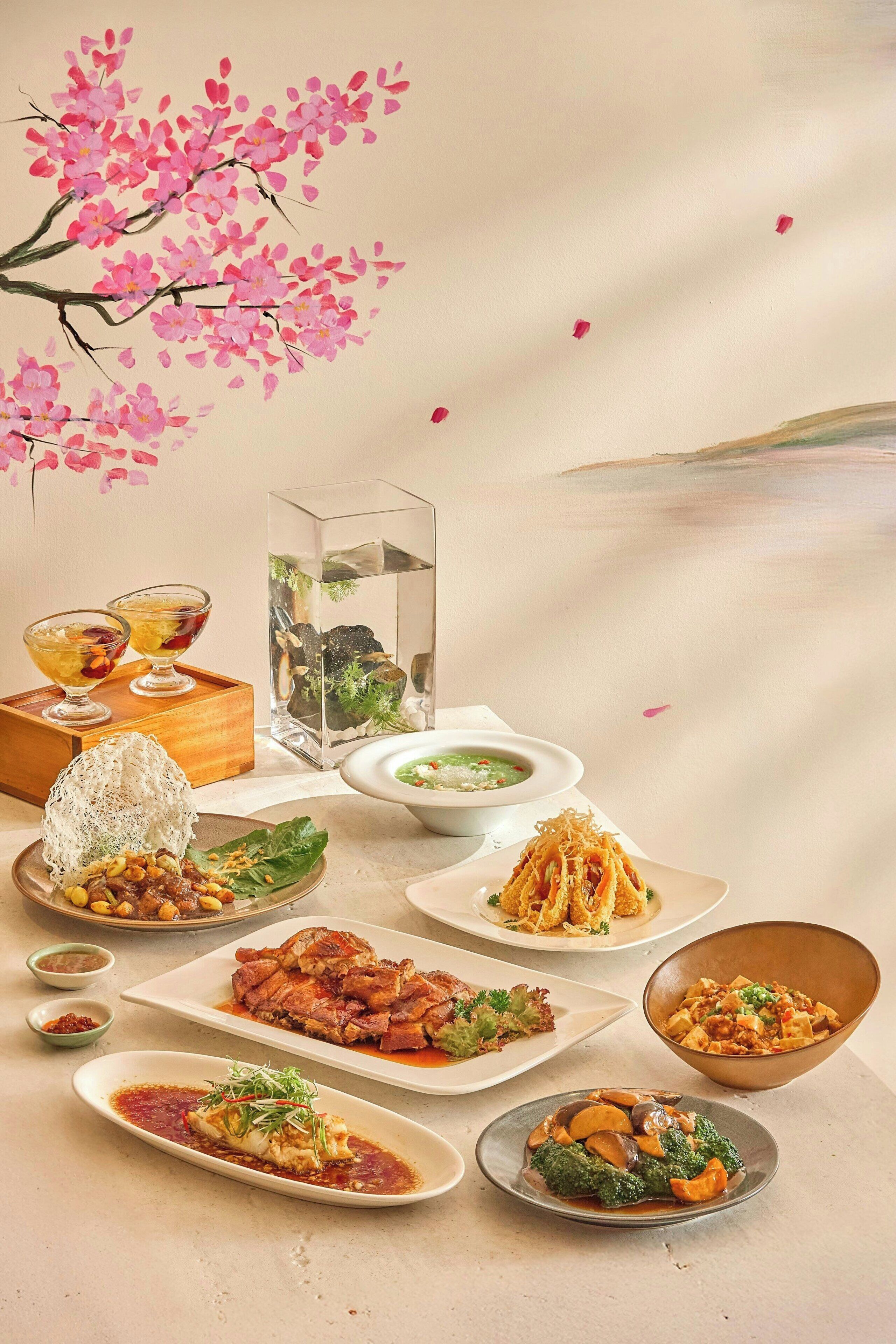 A table with various dishes, a bonsai tree, and a decorative painting of cherry blossoms.