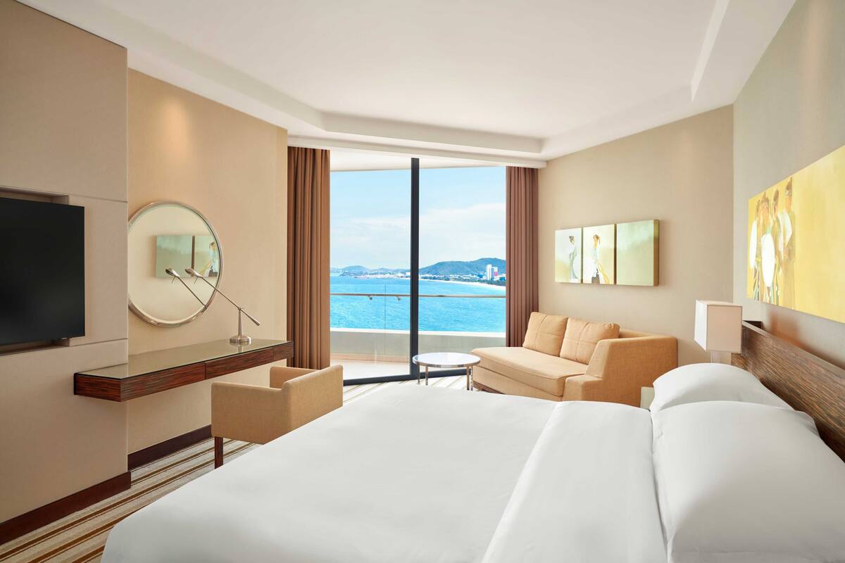 Une chambre d’hôtel avec un grand lit, un bureau, une chaise, une télévision et une vue sur la mer.