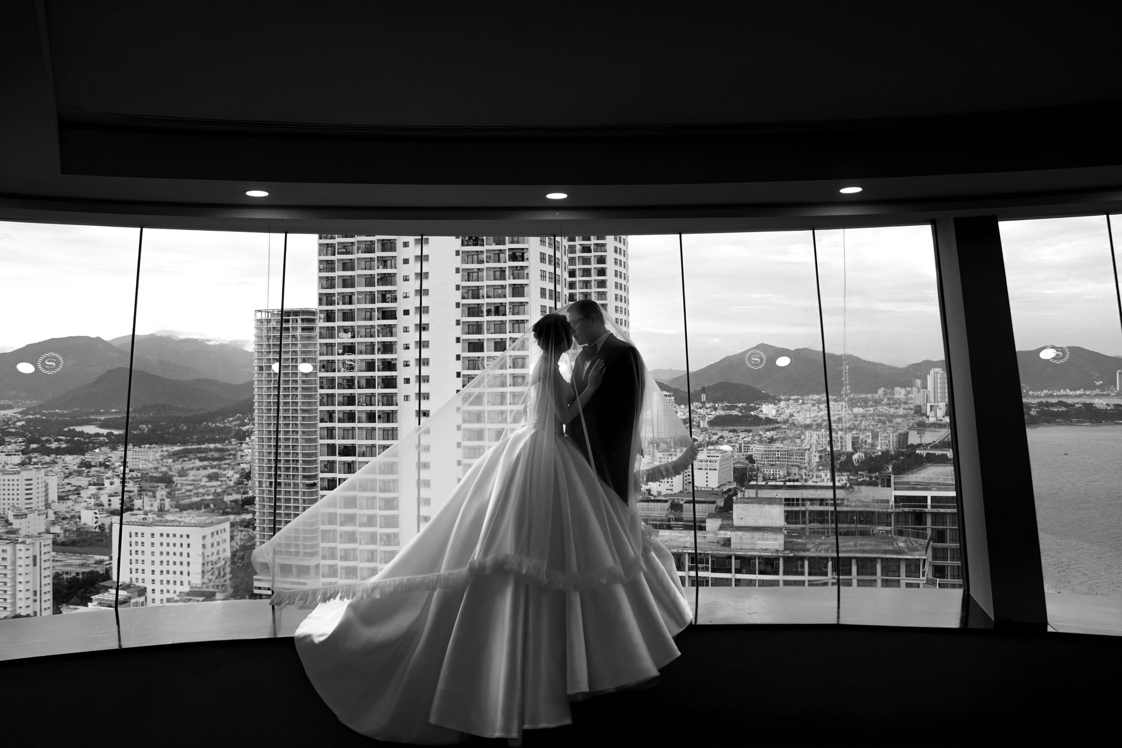 Ein Paar umarmt in einem Zimmer mit einem großen Fenster mit Blick auf eine Stadtlandschaft und Berge.