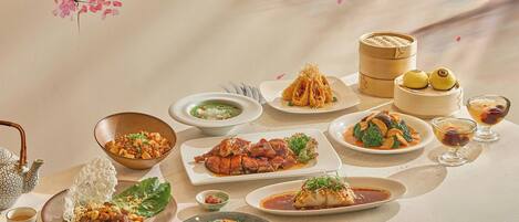A table with various dishes, including rice, soup, and meat, along with a teapot and a bamboo steamer.
