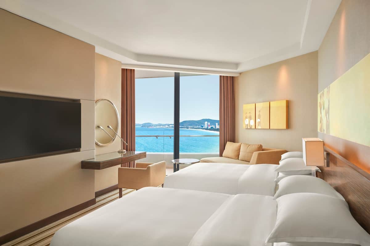 Une chambre d’hôtel avec deux lits, une télévision, un bureau et vue sur la mer.
