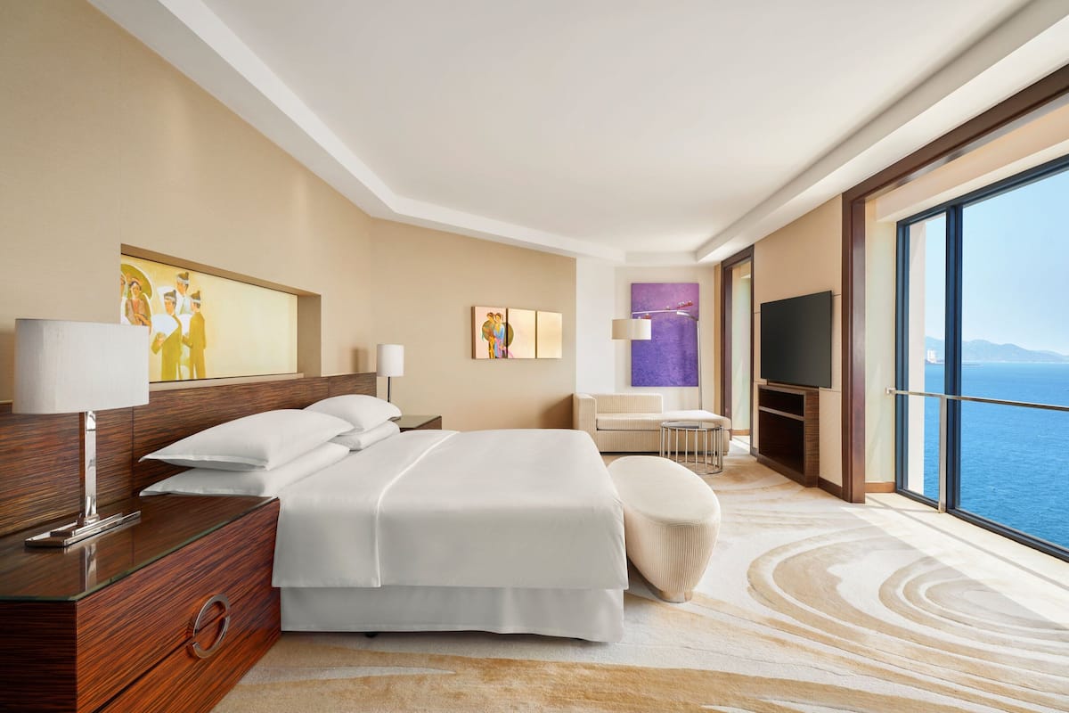 Une chambre d’hôtel moderne dotée d’un grand lit, d’un bureau, d’une chaise, d’une télévision et offrant une vue sur l’océan.