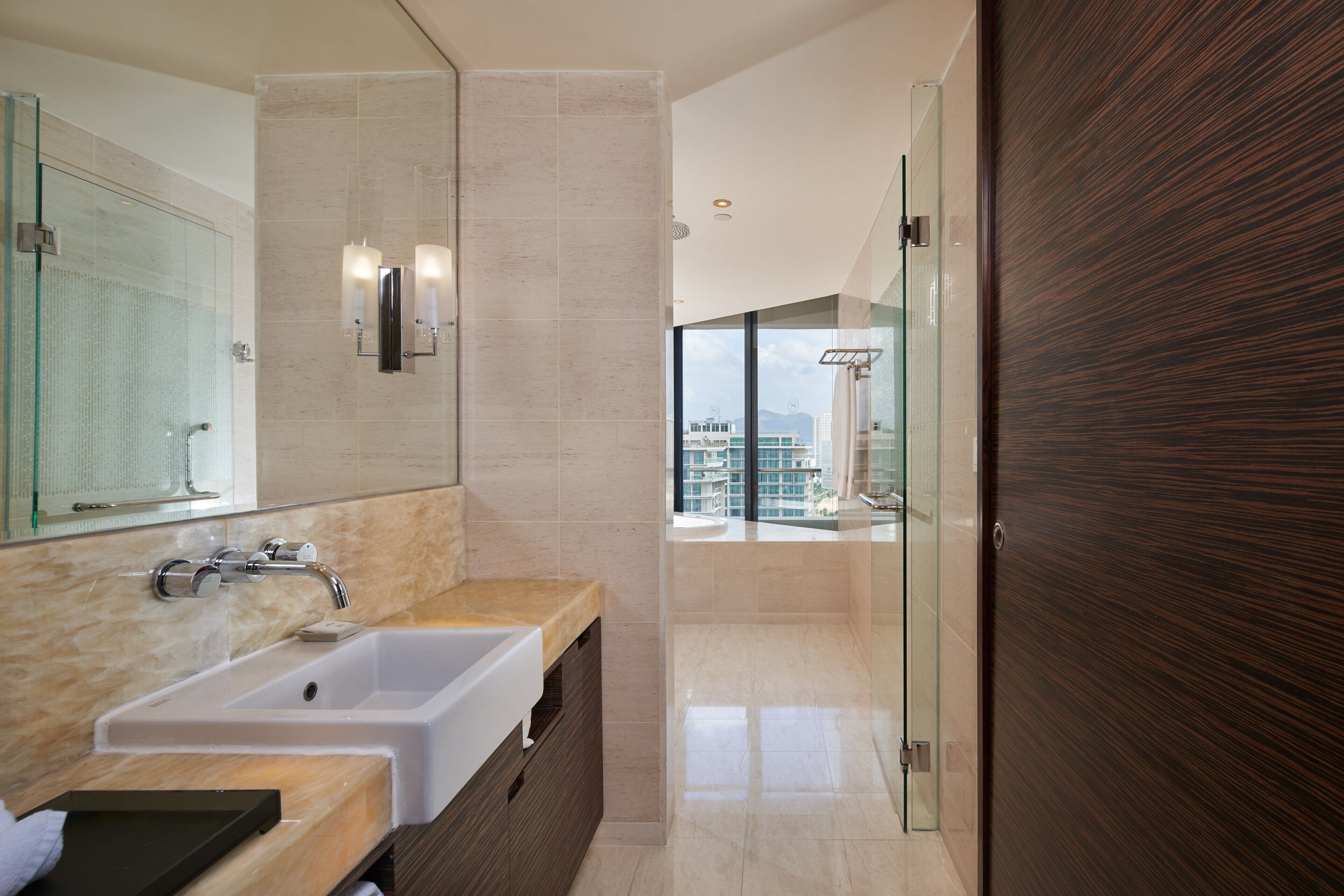 Un baño moderno con un espejo grande, un lavamanos blanco y una cabina de ducha con mampara de vidrio.