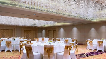 A banquet hall with round tables, white chairs with gold sashes, and a ceiling adorned with numerous white spherical decorations.