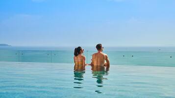 A couple sitting in an infinity pool with a view of the ocean.