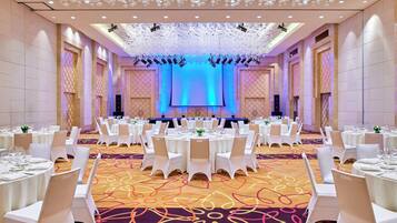 A banquet hall with round tables, white chairs, and a stage with blue lighting.
