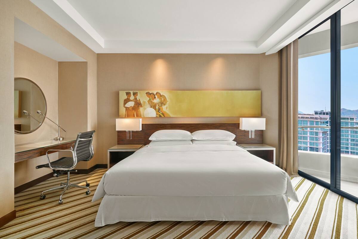 Une chambre d’hôtel avec un grand lit, un bureau avec une chaise, un miroir et un tableau au mur.