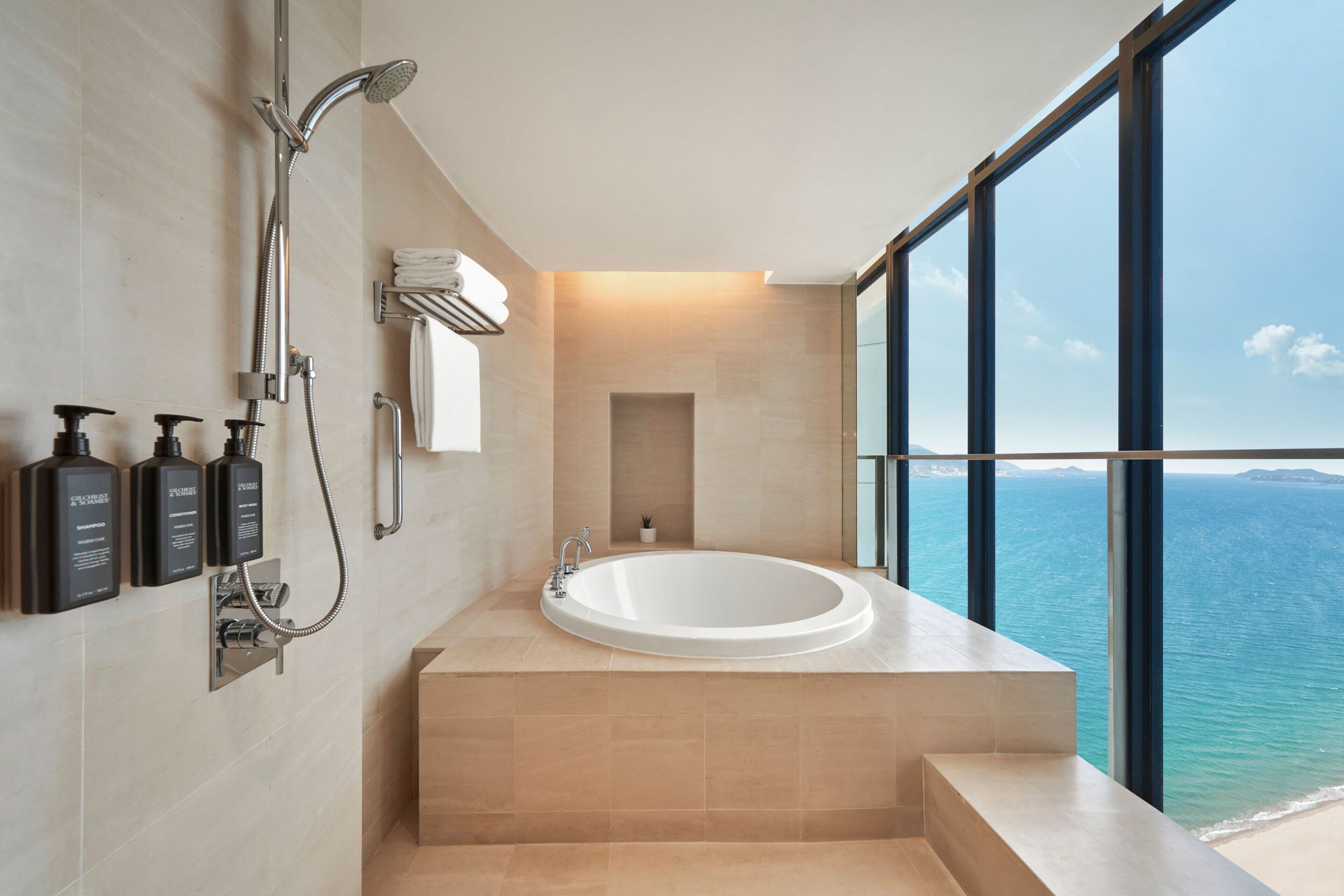 A modern bathroom with a large bathtub, a showerhead, and a view of the ocean through large windows.