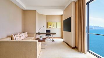 Habitación de hotel moderna con un ventanal grande, un sofá, un escritorio con computadora y un televisor de pantalla plana.