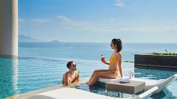 Una pareja en una piscina con un flotador de cisne, una bebida y vistas al mar.