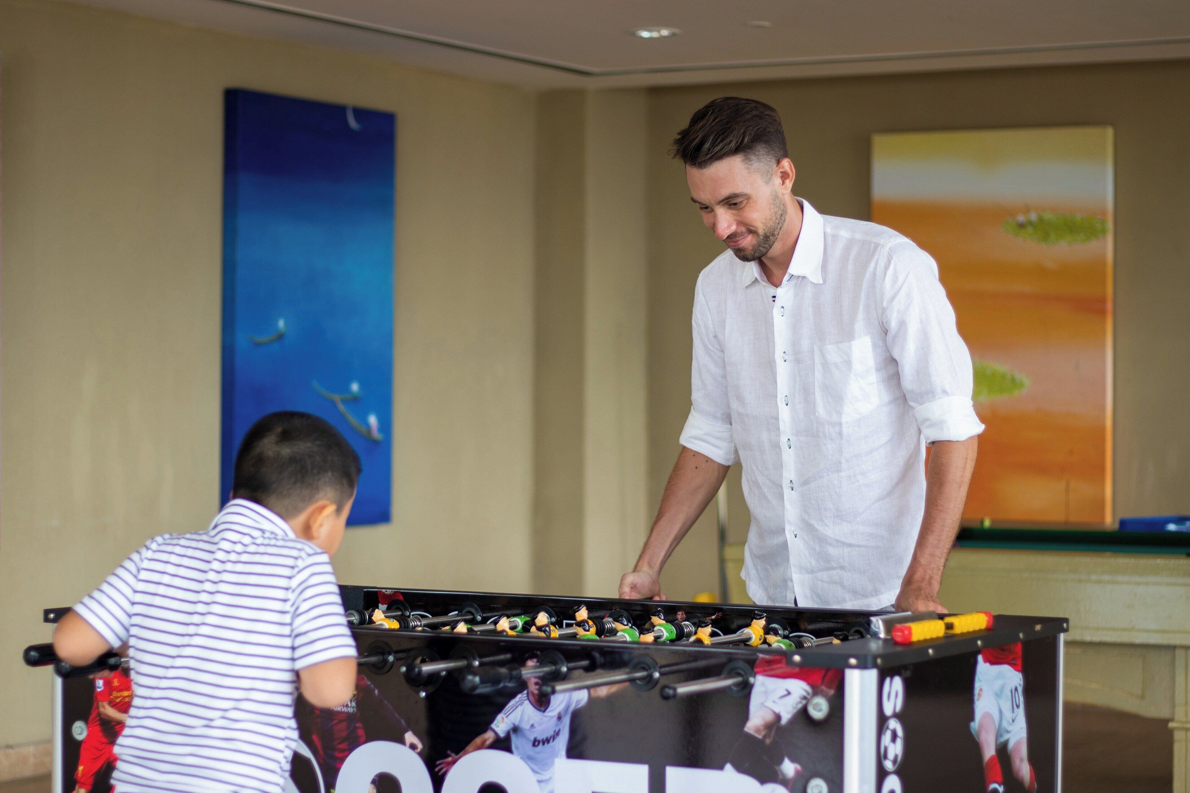 A foosball table in a room with a large painting on the wall and a pool table in the background.