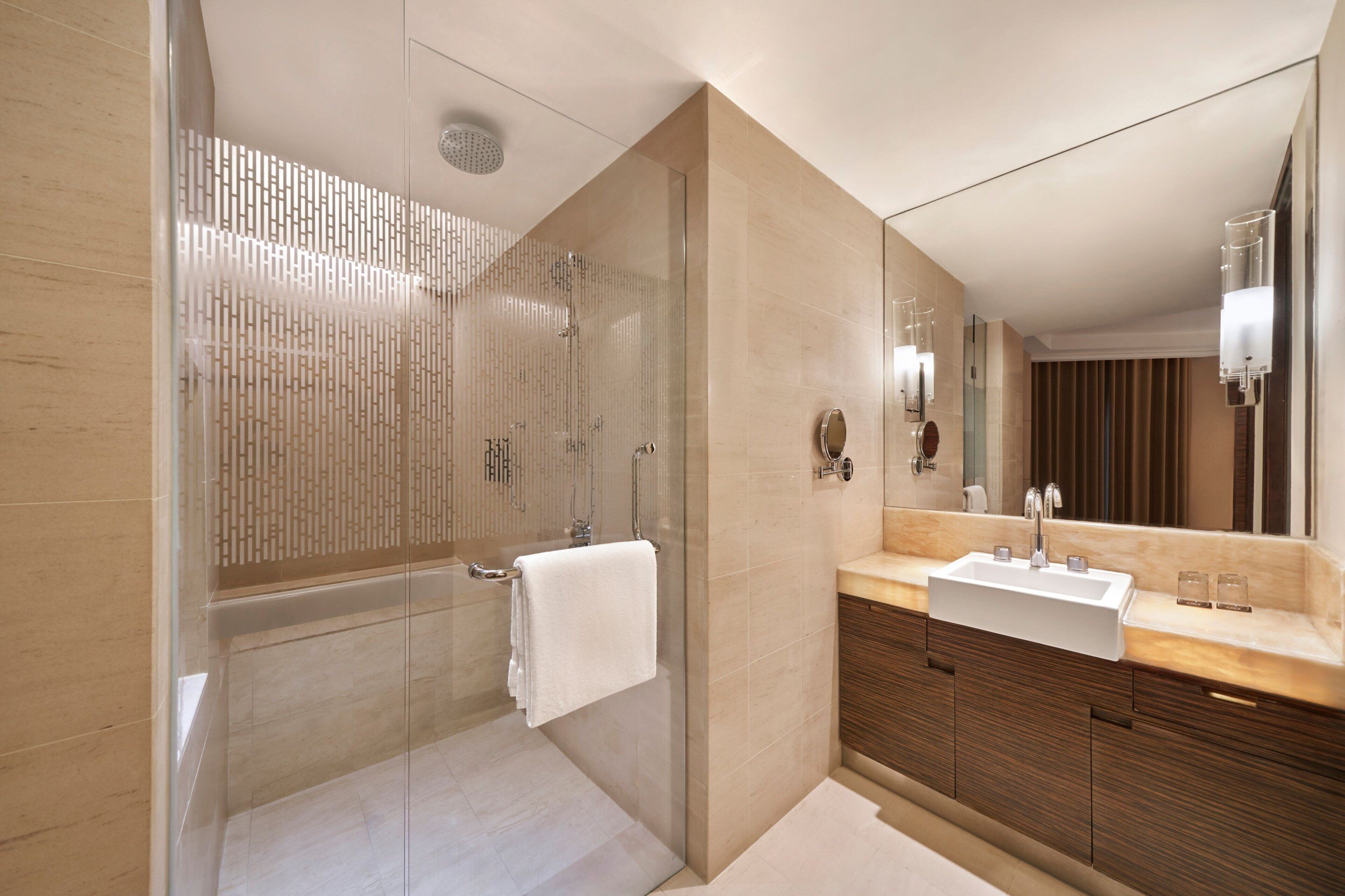 A modern bathroom with a glass-enclosed shower, a large mirror, and a wooden vanity with a sink.