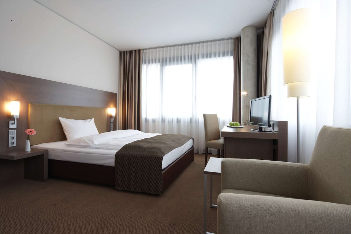 Ein Hotelzimmer mit einem Bett, einem Schreibtisch mit Computer, einem Stuhl und einer Lampe.