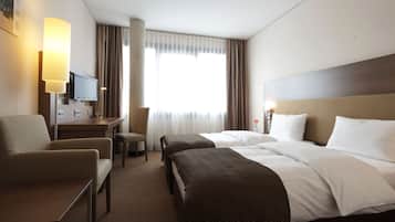Een hotelkamer met twee bedden, een bureau, een stoel, een televisie en een groot raam met gordijnen.