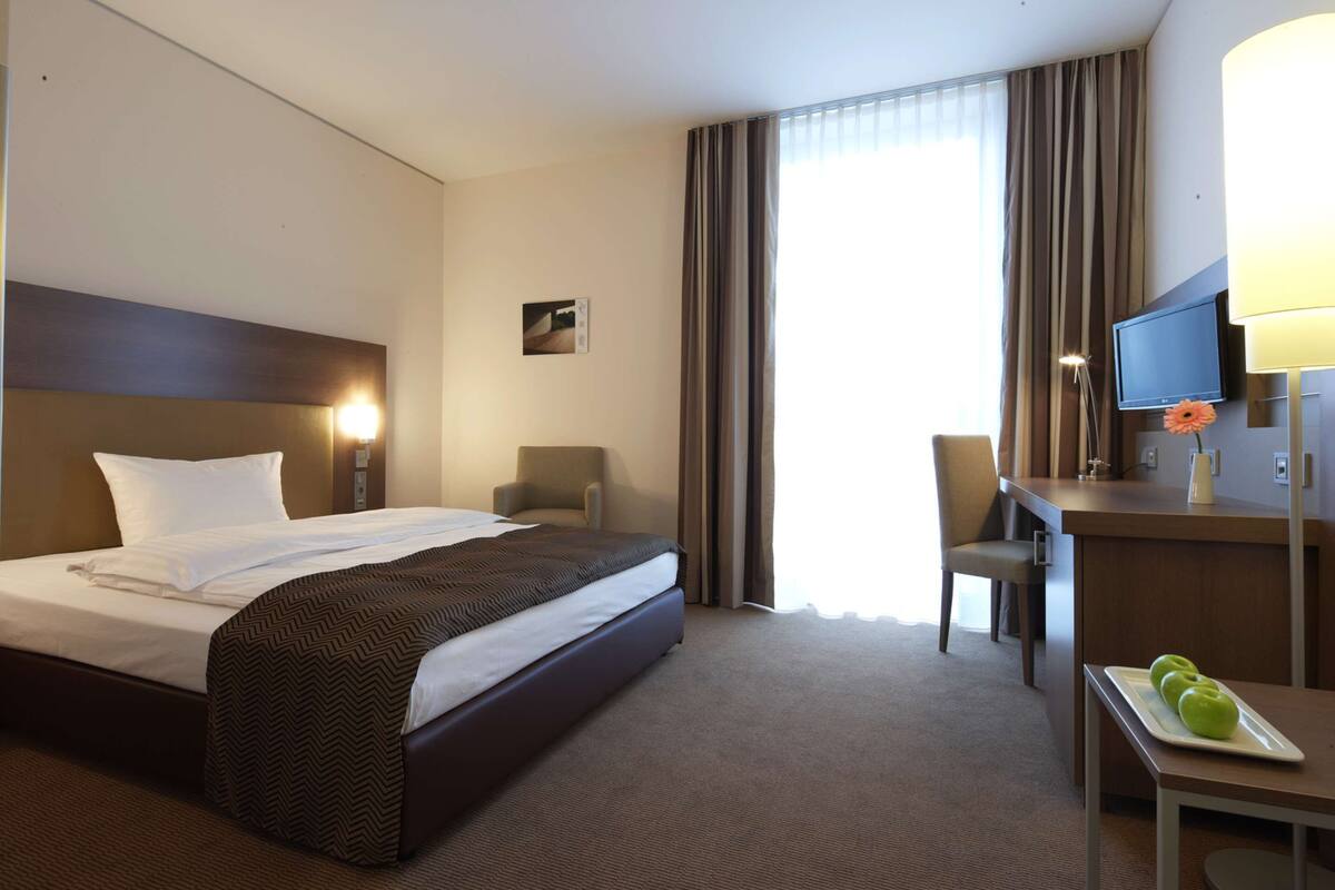 Ein Hotelzimmer mit einem großen Bett, einem Schreibtisch mit Lampe, einem Fernseher und einem kleinen Tisch mit Äpfeln.