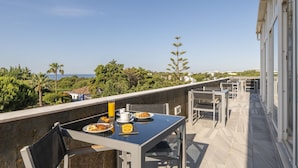 A balcony with a table set for breakfast, overlooking a scenic view of the sea and greenery.