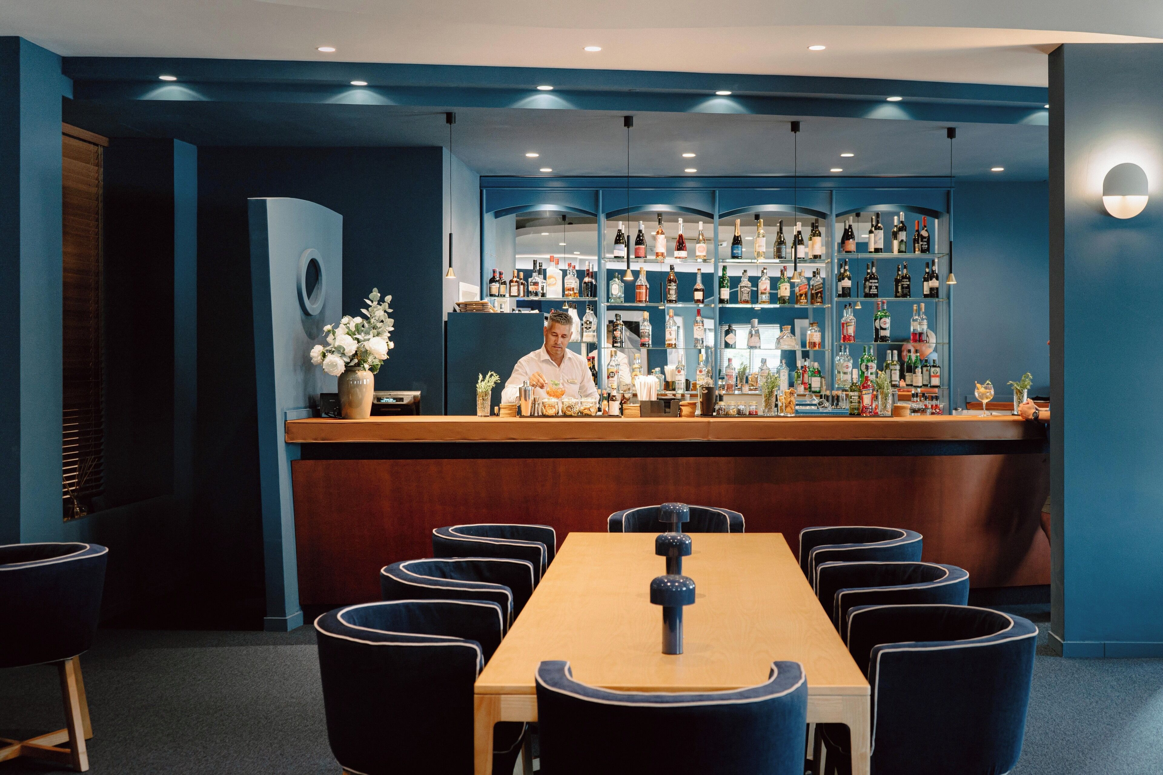 A bar area with a bartender, a wooden bar counter, and a seating area with round tables and chairs.