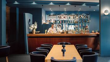 A bar area with a bartender, a wooden bar counter, and a seating area with round tables and chairs.