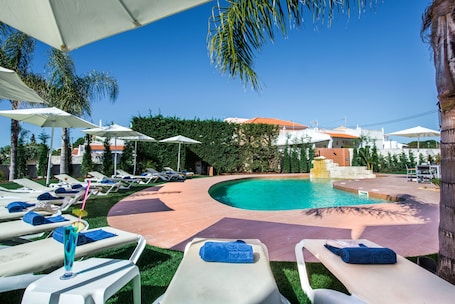 Una piscina al aire libre, sombrillas, sillones reclinables de piscina