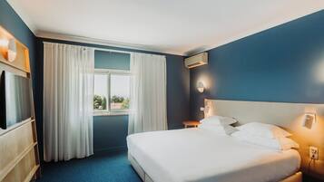 Una habitación de hotel con cama, televisión, ventana con cortinas y aire acondicionado.