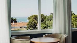 A room with a large window overlooking a coastal view, featuring two chairs and a small table.