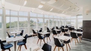 A spacious dining area with tables and chairs arranged for guests, large windows offering a view of the outdoors, and a modern ceiling design.