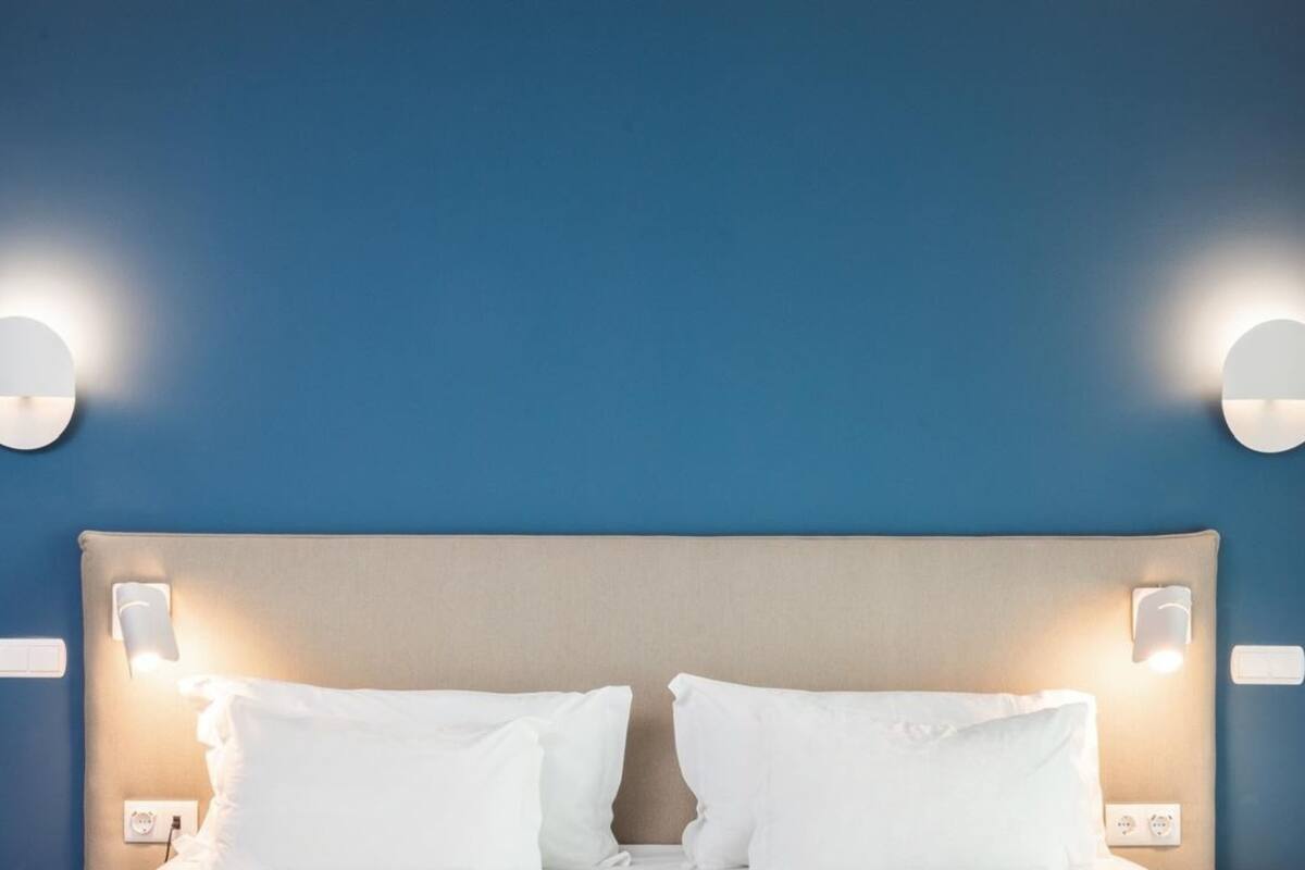 A hotel room with a blue wall, a beige headboard, and two wall-mounted light fixtures.