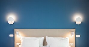 Een bed met witte lakens, een beige hoofdbord en twee wandlampen op een blauwe muur.
