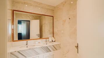 A bathroom with a marble vanity, two sinks, a large mirror, and a door leading to another room.