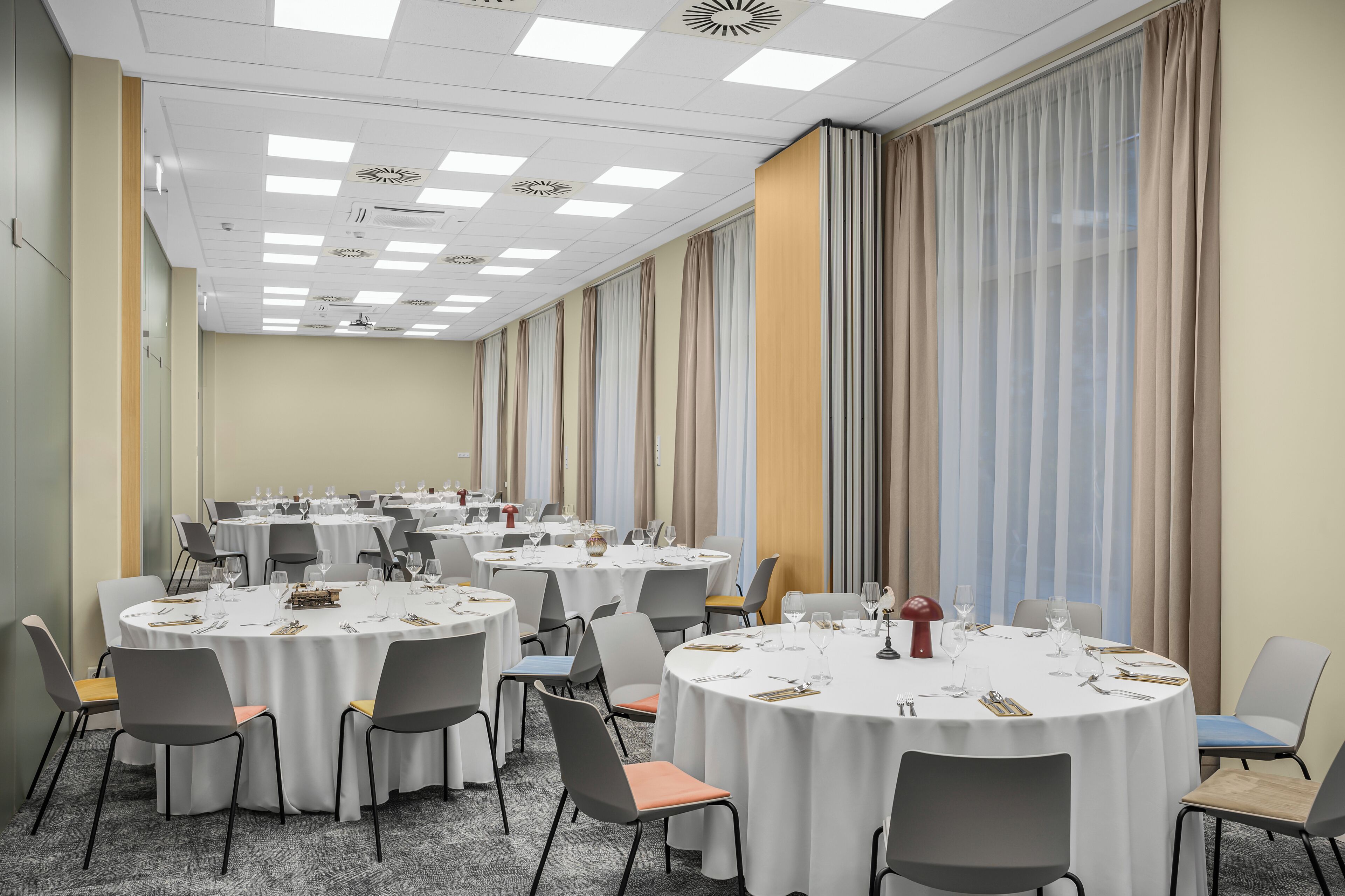 A conference room with multiple round tables, each set with white tablecloths, chairs, and dining utensils.