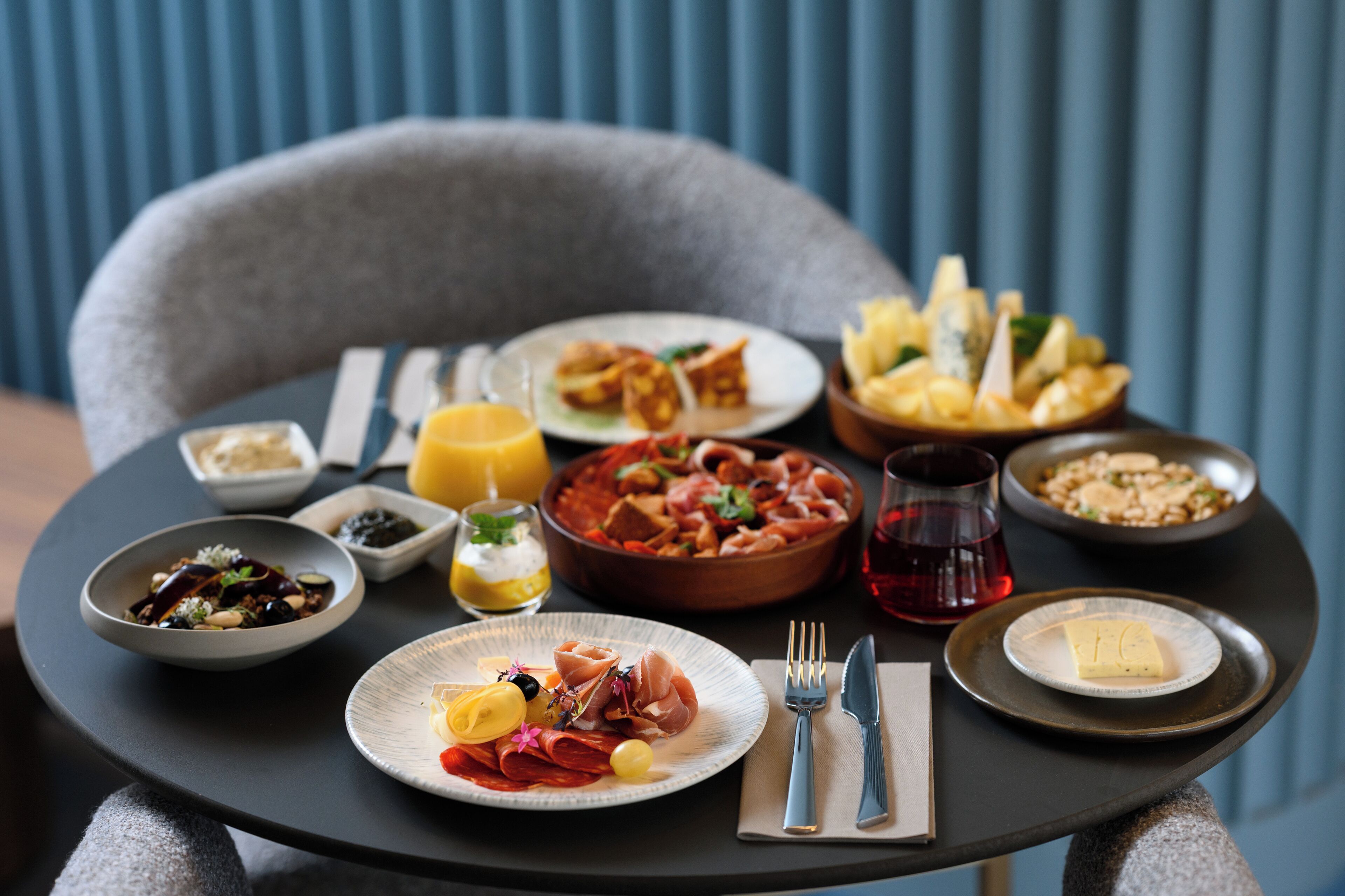 A table set with various dishes, including a bowl of pasta, a plate of cured meats, and a bowl of bread.