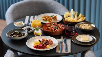 A table set with various dishes, including a bowl of pasta, a plate of cured meats, and a bowl of bread.