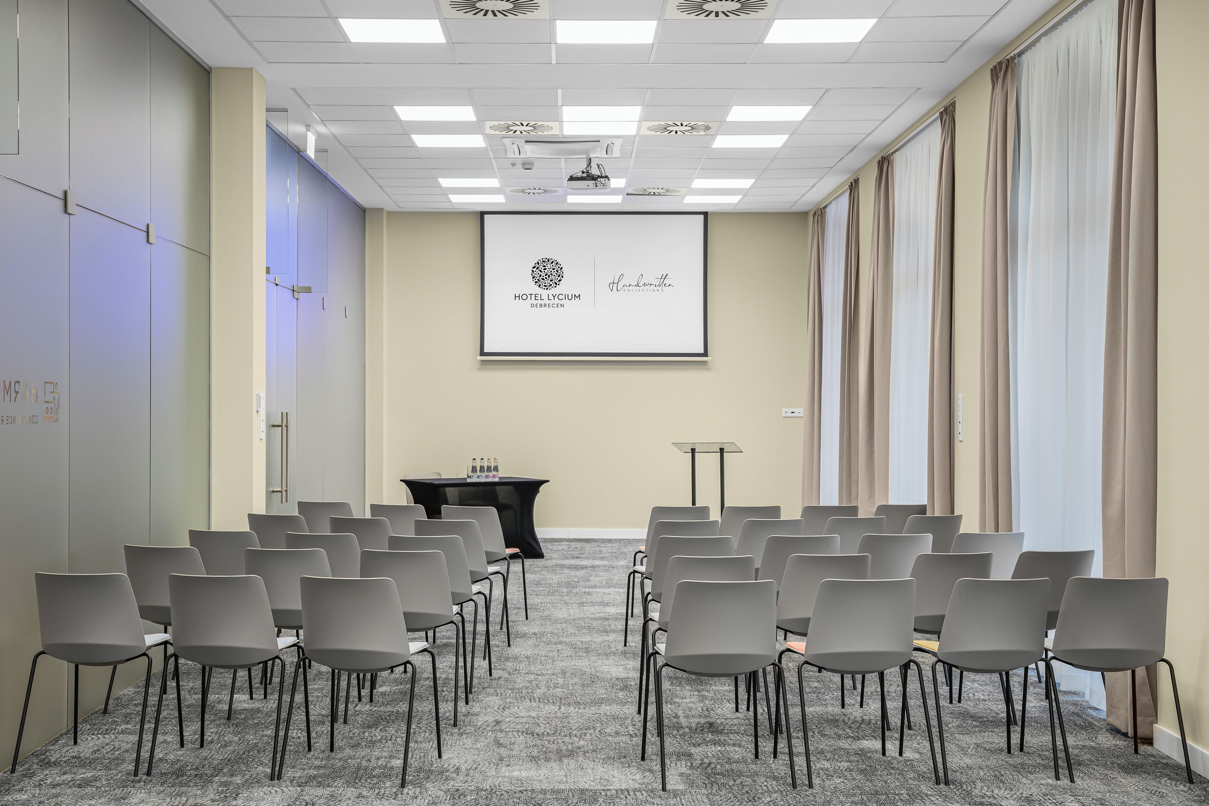 A conference room with rows of chairs, a projector screen displaying a logo, and a podium.