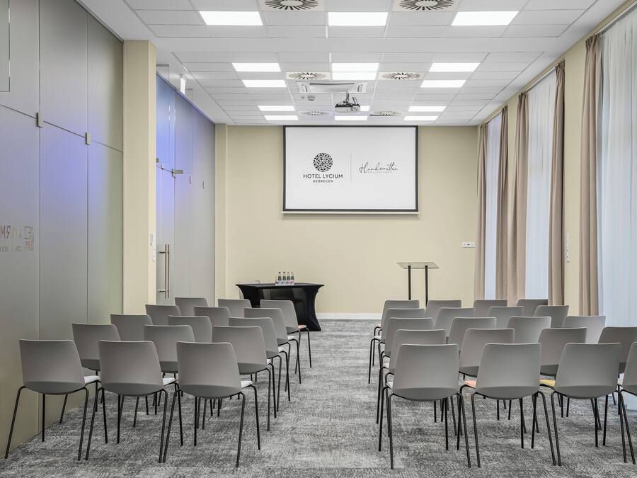 A conference room with rows of chairs, a projector screen displaying a logo, and a podium.