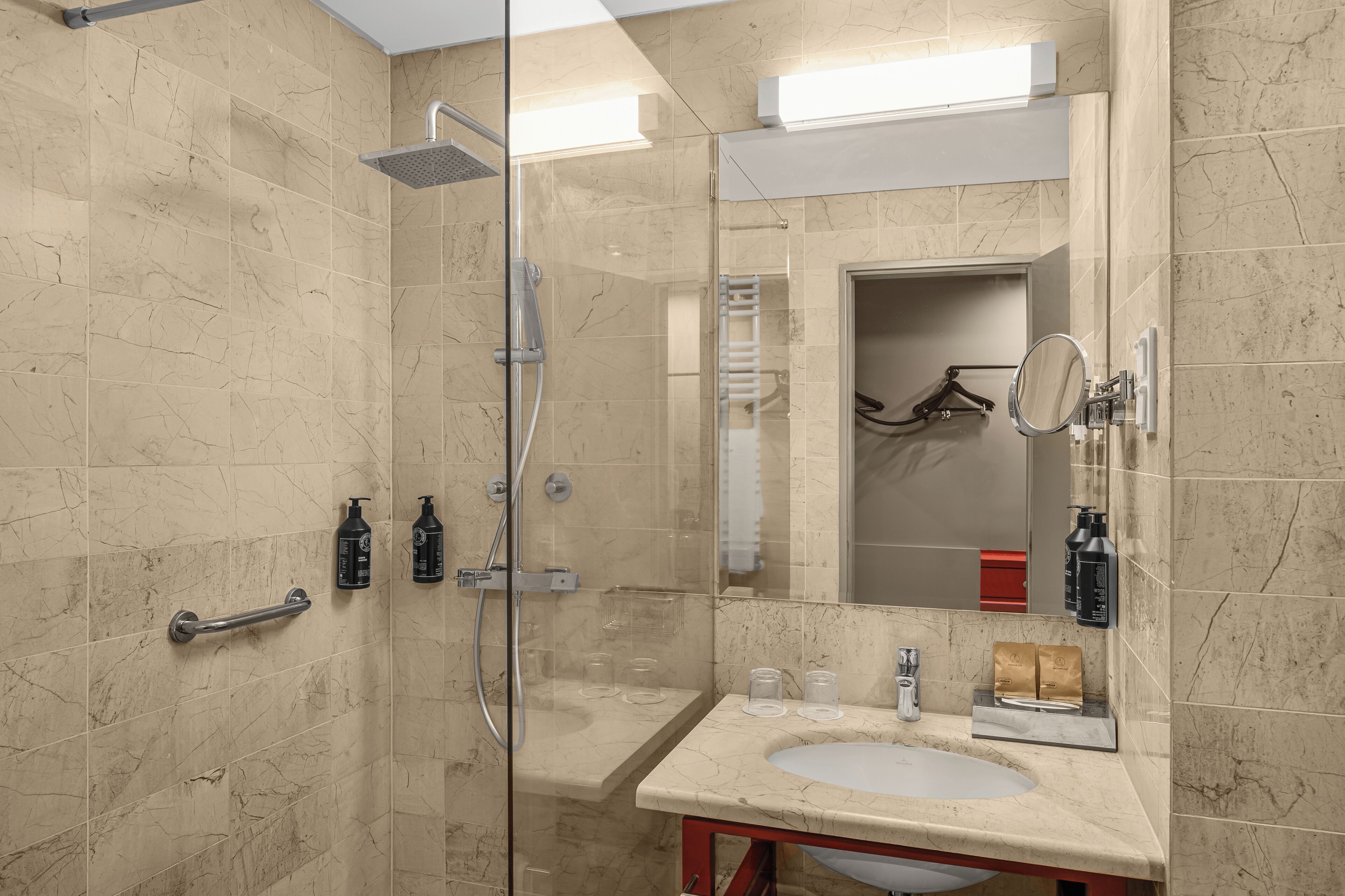 A modern bathroom with a glass-enclosed shower, a sink with a mirror, and toiletries on the countertop.