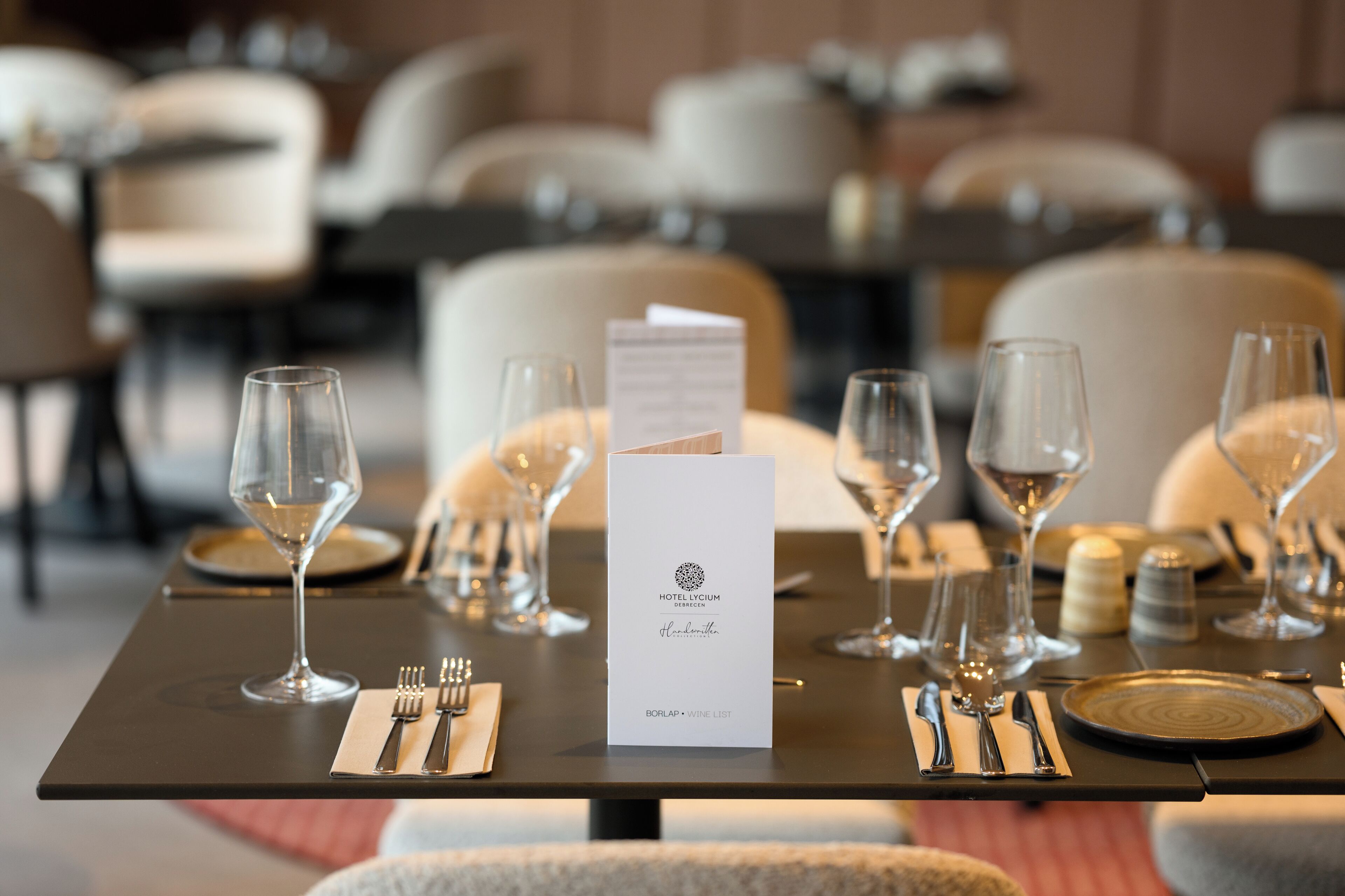 A dining table set with wine glasses, plates, and cutlery, with a menu in the center.