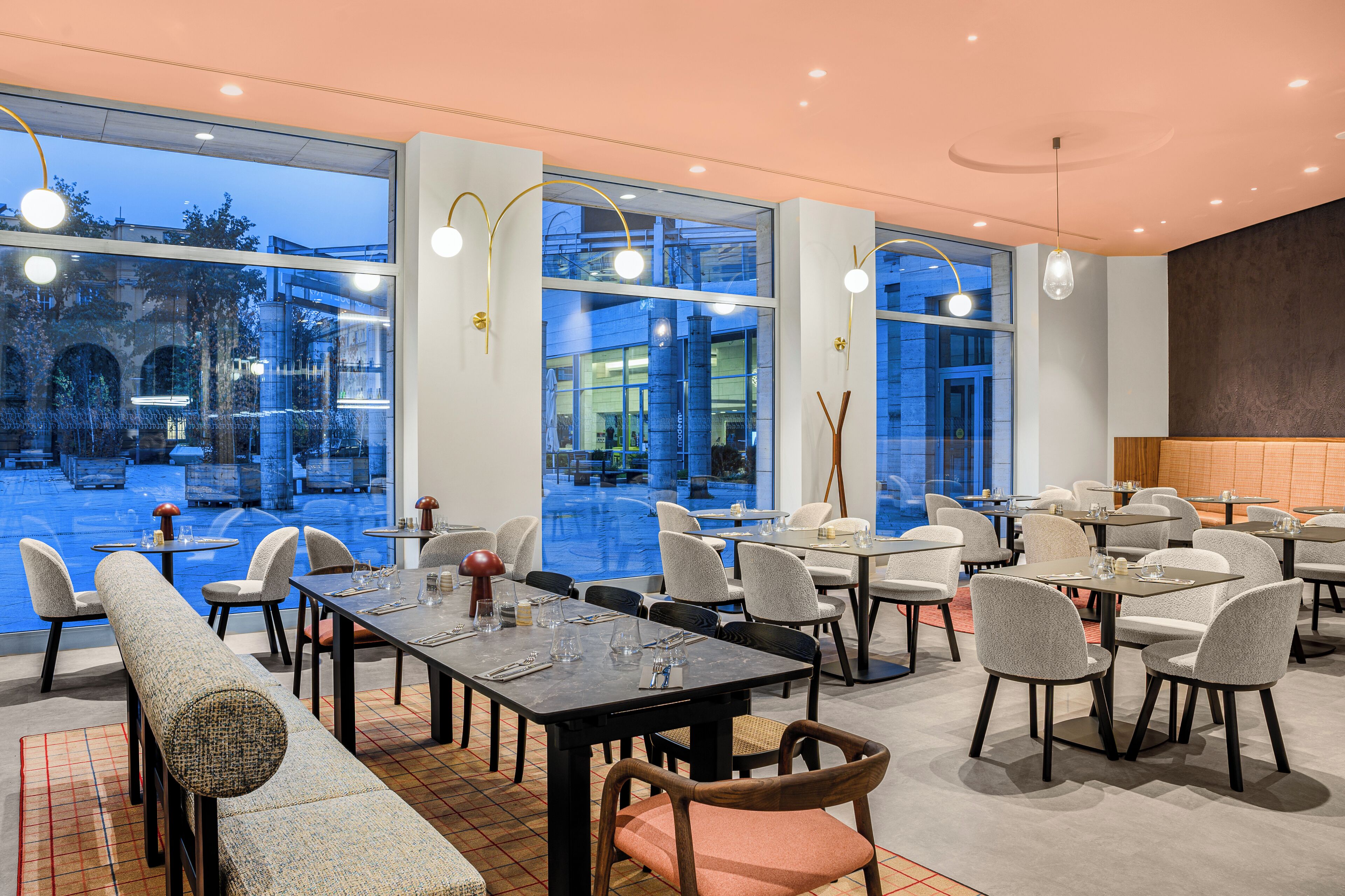 Un restaurante moderno con amplios ventanales, varias mesas y sillas.