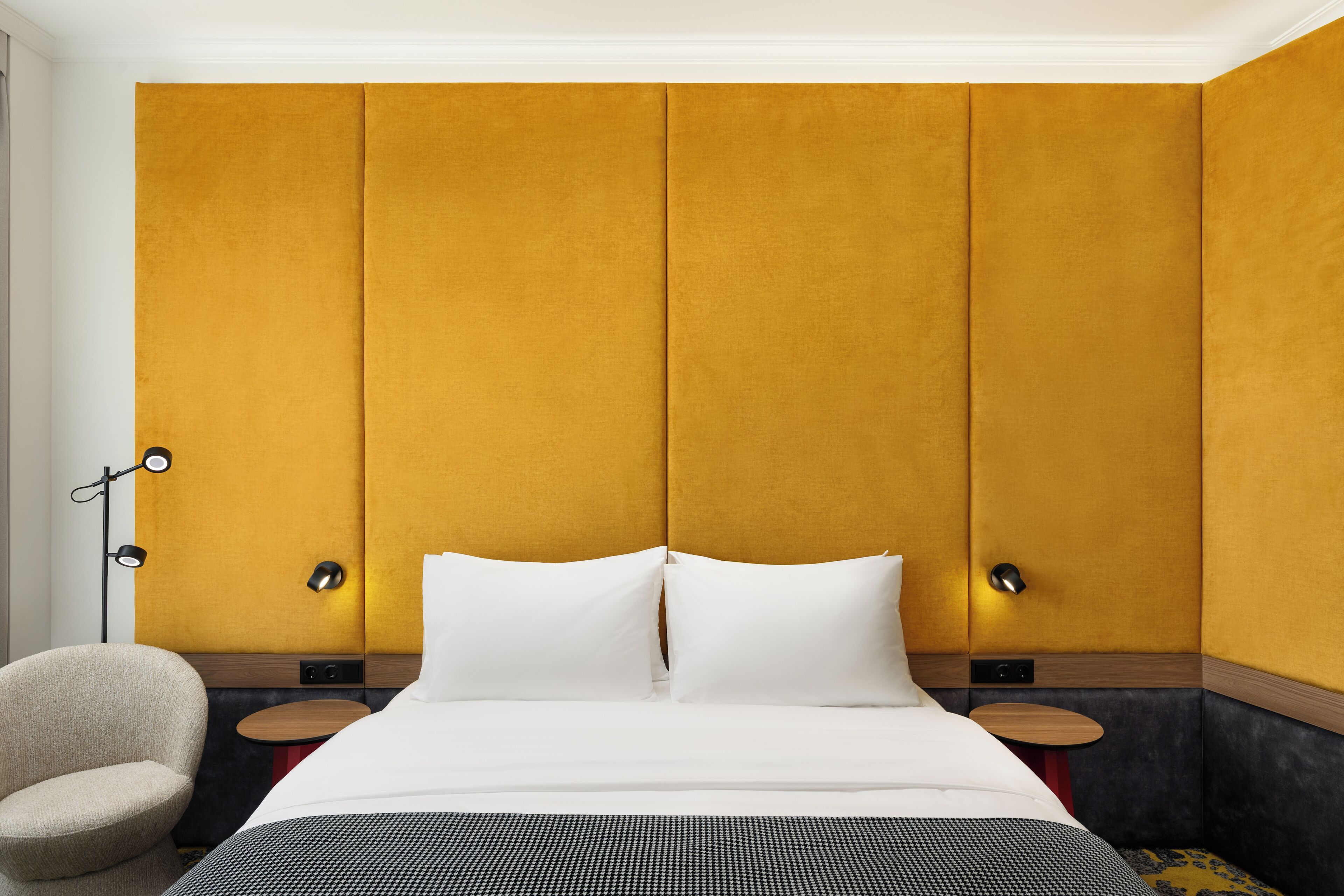 A hotel room with a large bed, a chair, a bedside table, and a wall with a textured panel design.